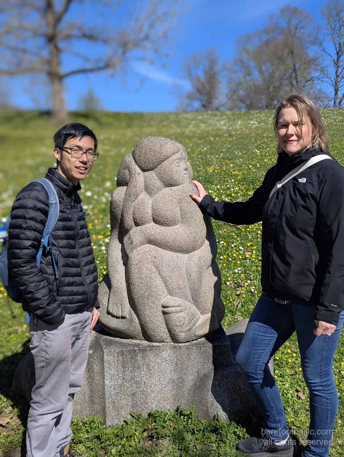 Daiga and a guest beside the seated mother-and-child sculpture at the Hill of Dainas, Turaida