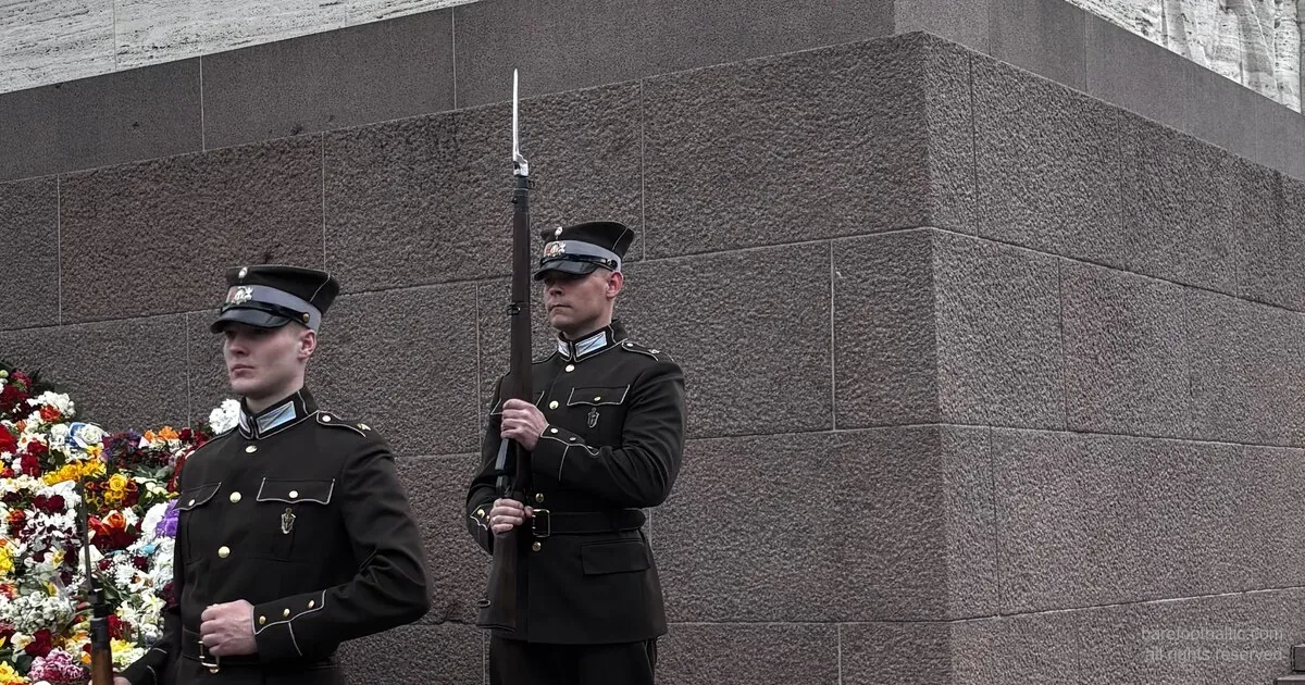Latvian Army honor guard at the Freedom Monument with a wall of flowers laid against the base, Riga, on Restoration of Independence Day