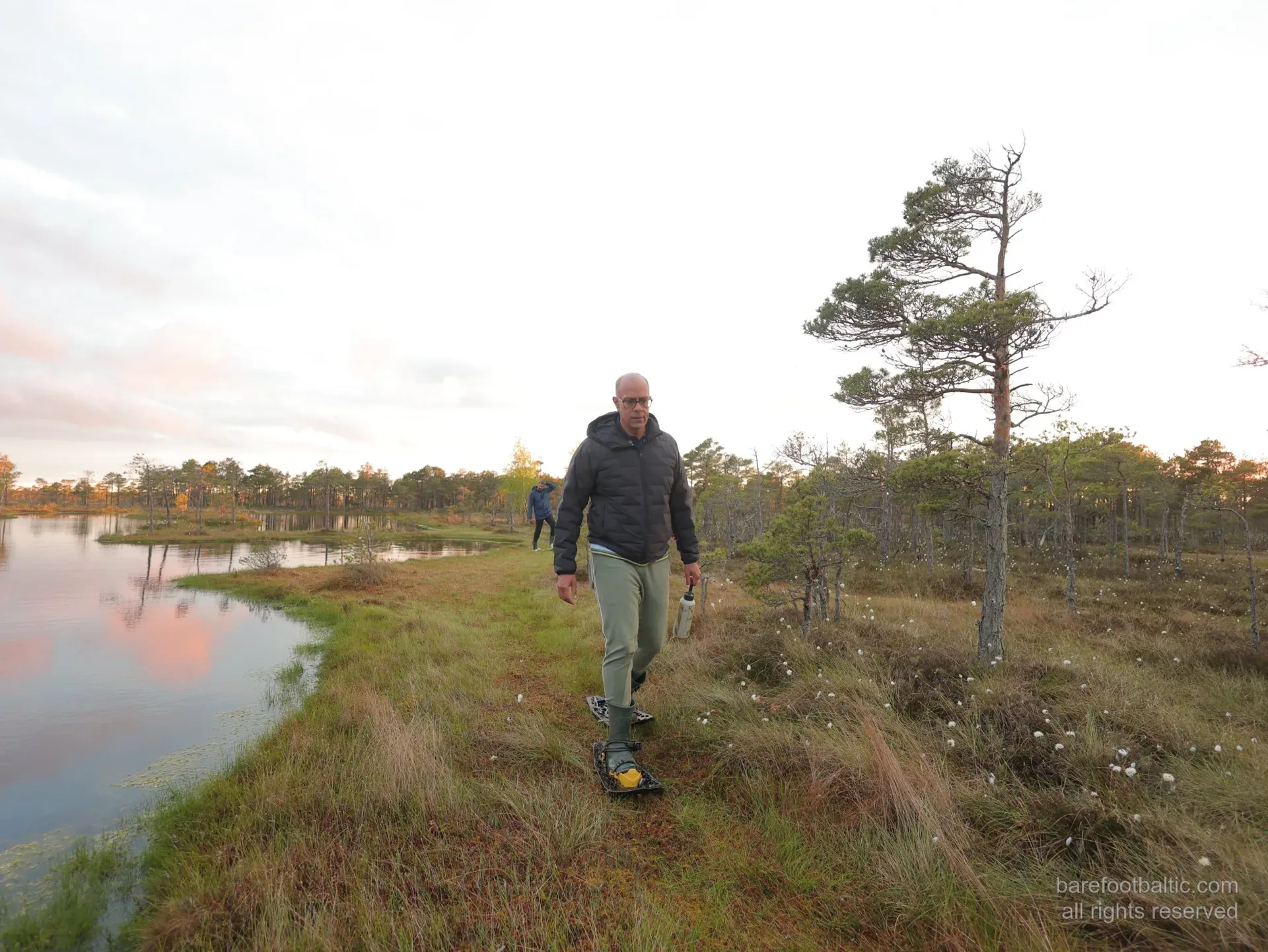 A guest in bog shoes beside a pink-lit bog pool