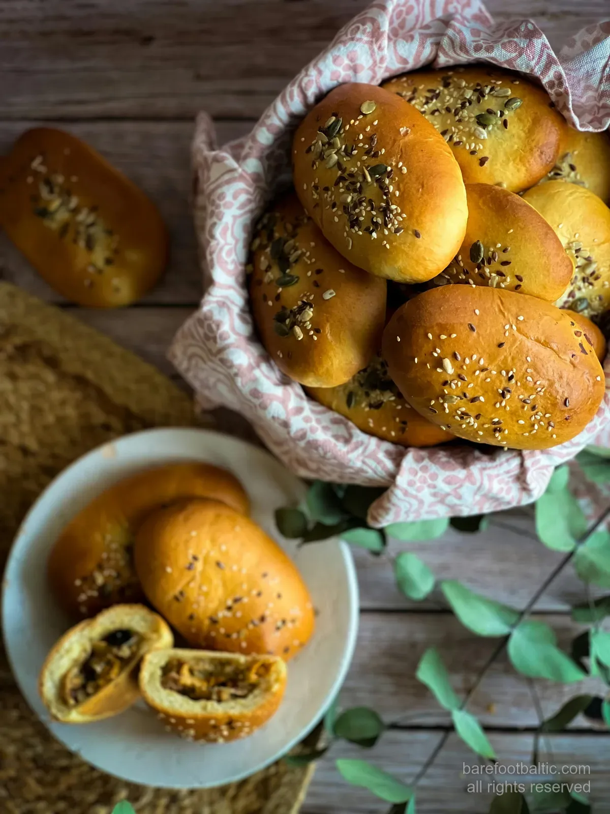 A basket of golden Latvian pīrāgi sprinkled with seeds, traditional small filled buns