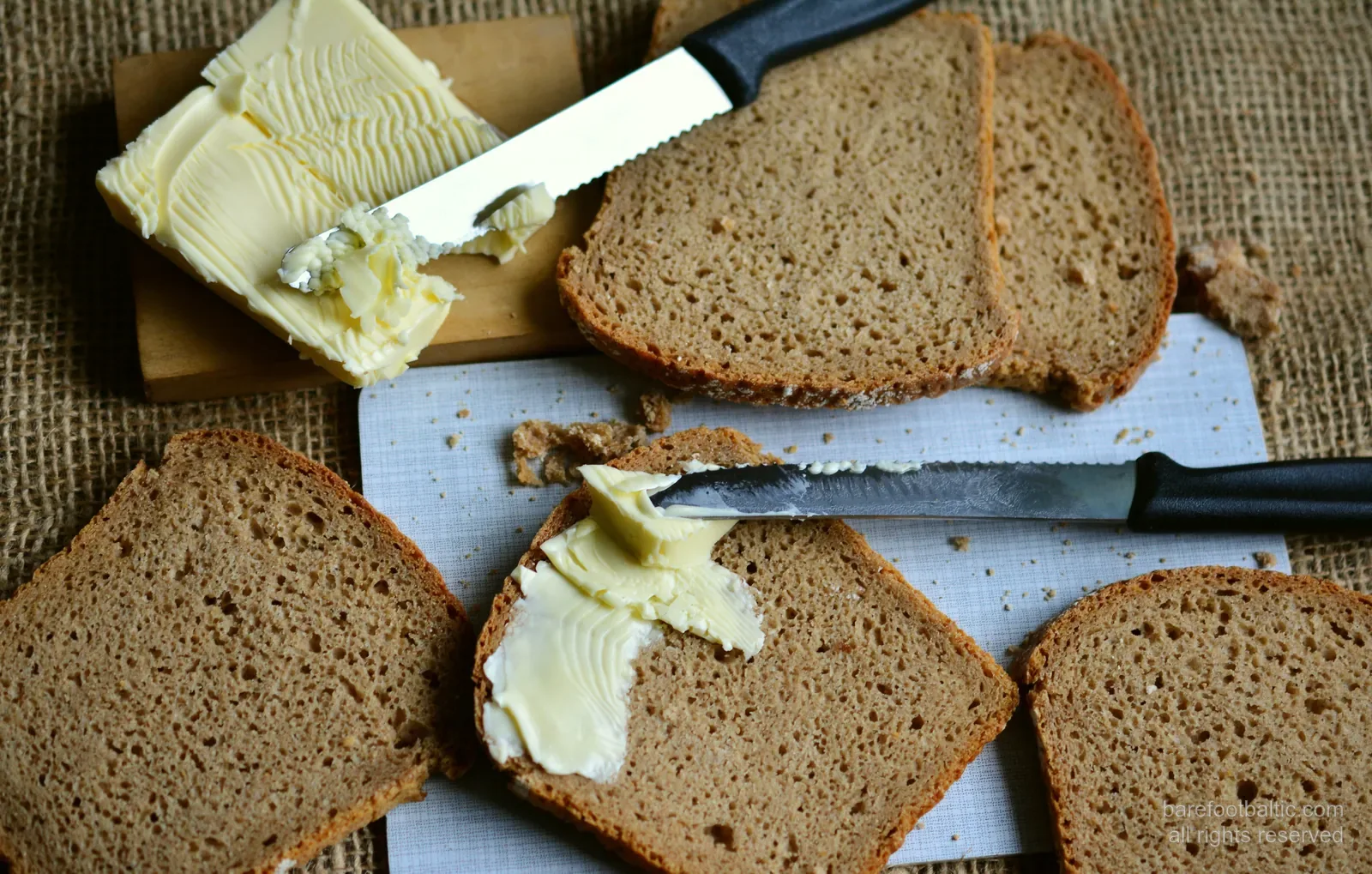 Slices of rupjmaize Latvian rye bread with butter and a knife on burlap