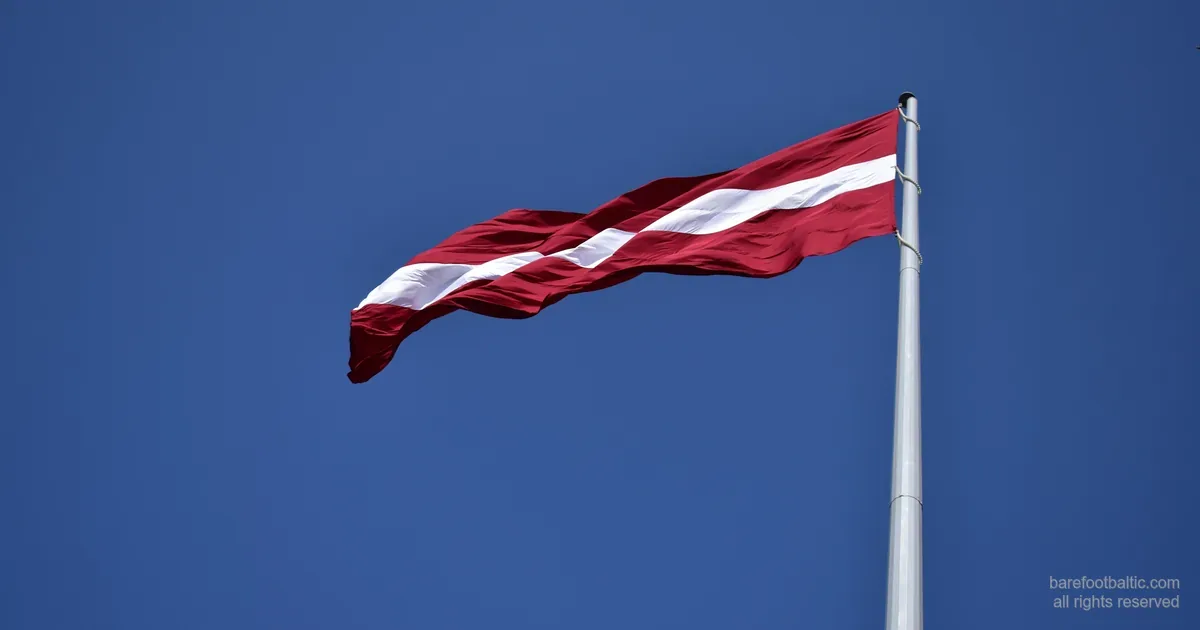 The Latvian flag — carmine red with a white band — flying against a blue sky.